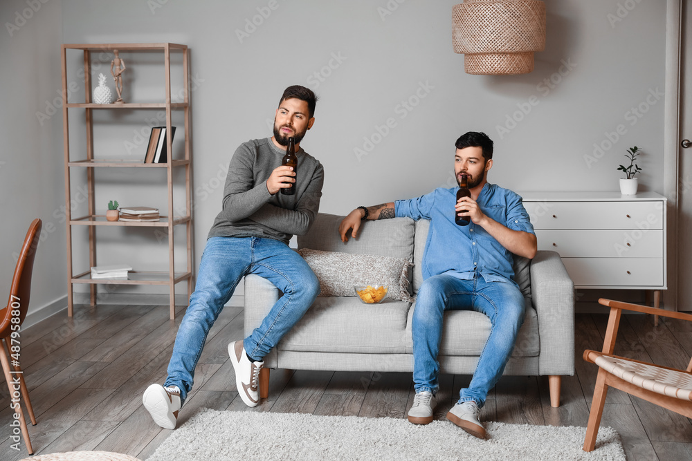 Male friends drinking beer on sofa at home