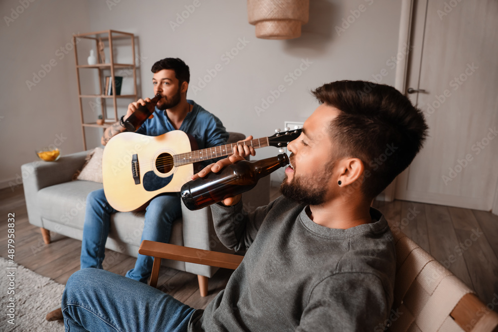 Young man drinking beer with friend at home, closeup