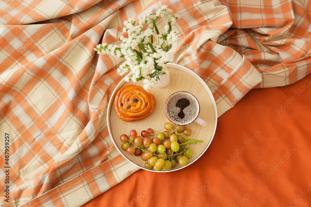 Tray with delicious breakfast and beautiful flowers on comfortable bed with plaid