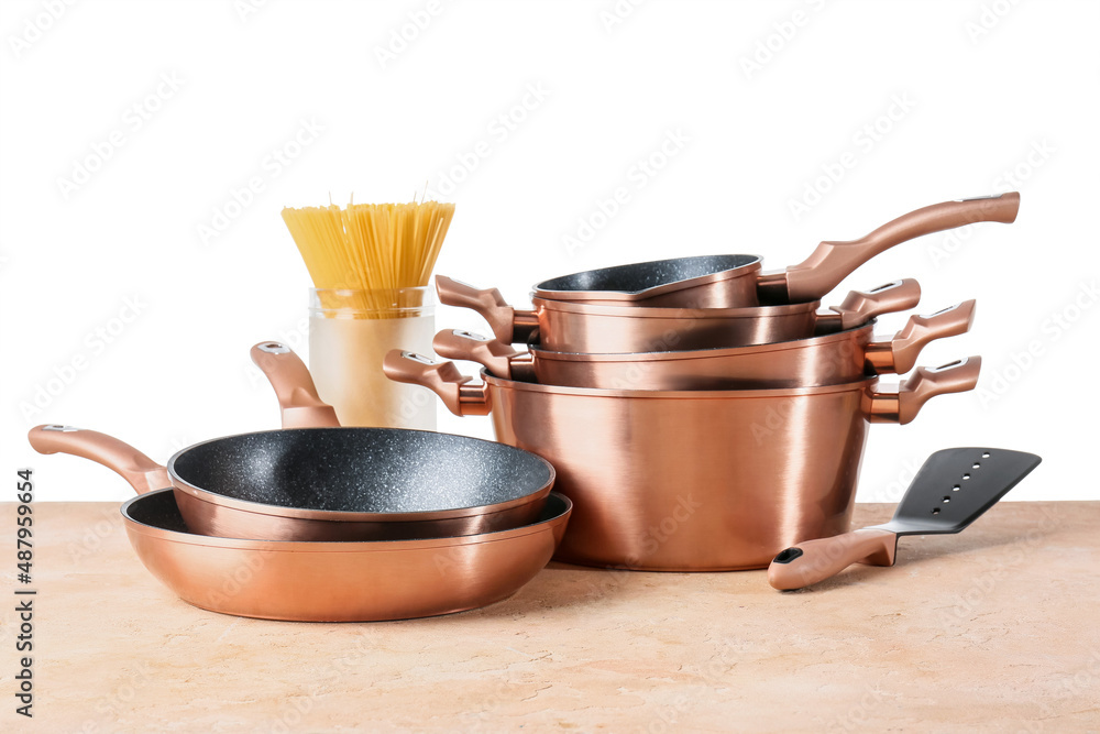 Set of copper kitchen utensils and jar with raw spaghetti on table against white background