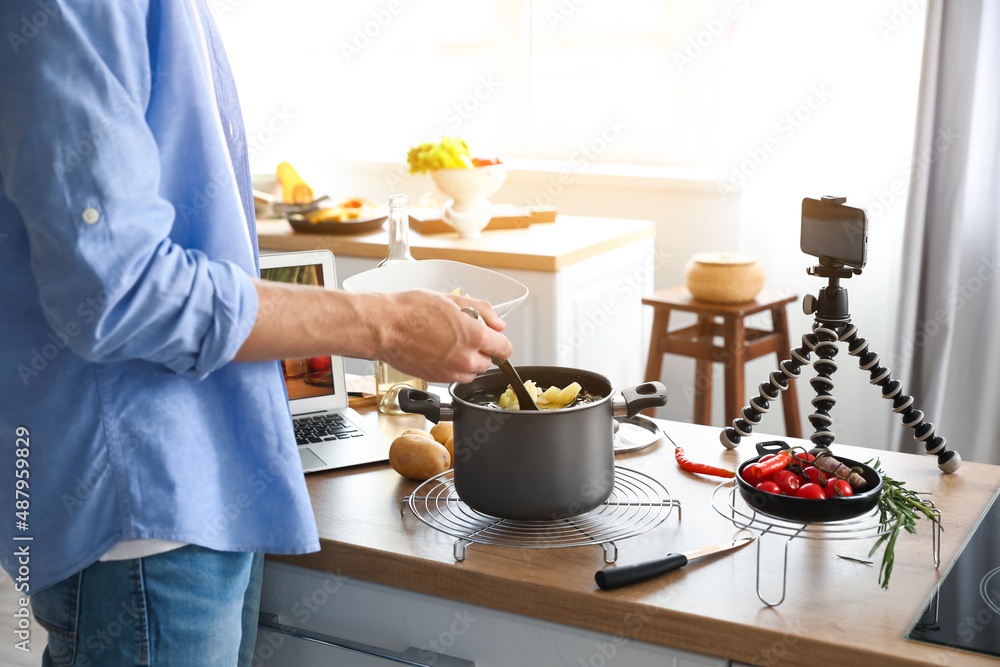 Young man pouring soup into bowl in kitchen