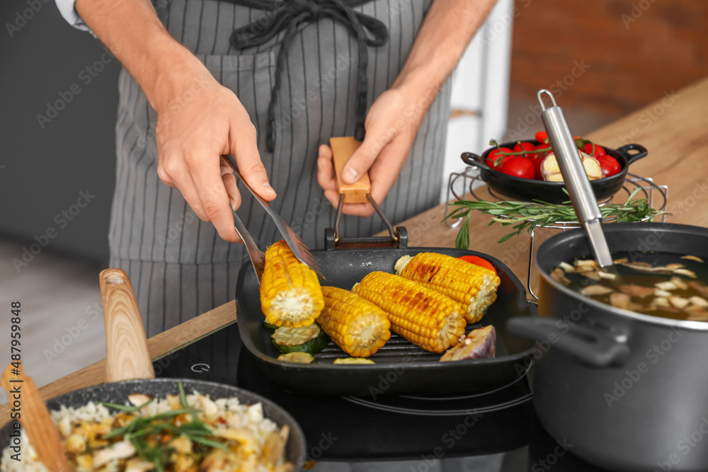 Young man frying corn in kitchen, closeup