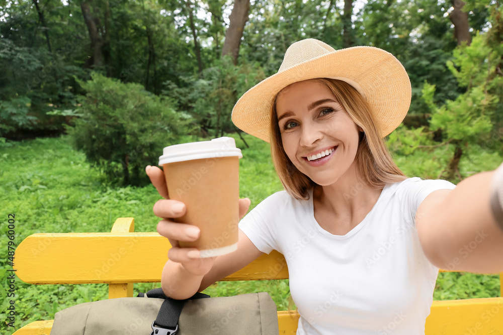 Female tourist with coffee taking selfie while sitting on bench in park