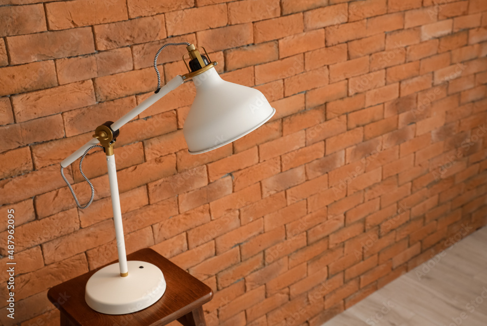 White lamp on wooden stool near brick wall