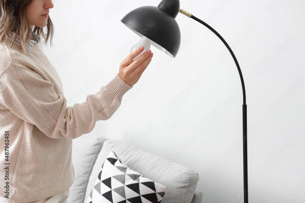 Woman changing light bulb in standard lamp at home