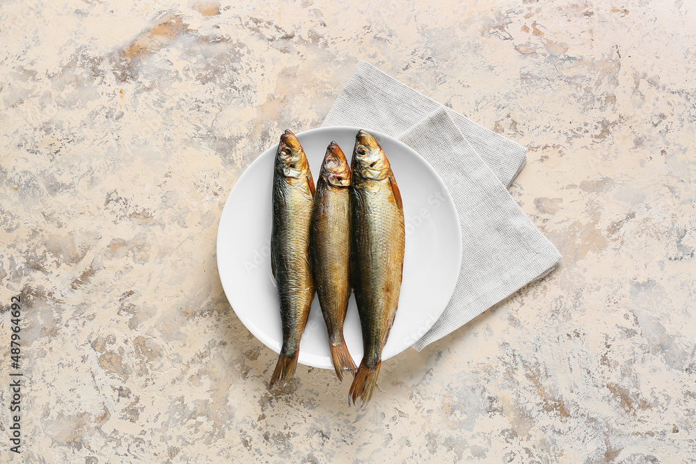 Plate with smoked herring fishes on beige background