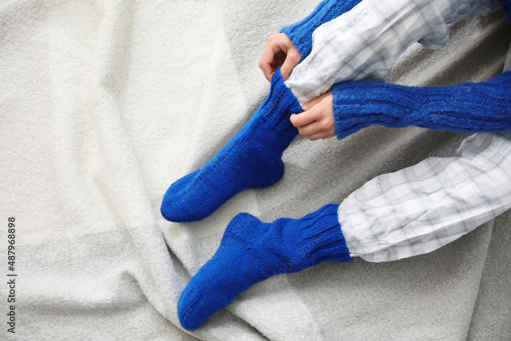 Woman sitting on plaid and adjusting warm socks, closeup. Concept of heating season