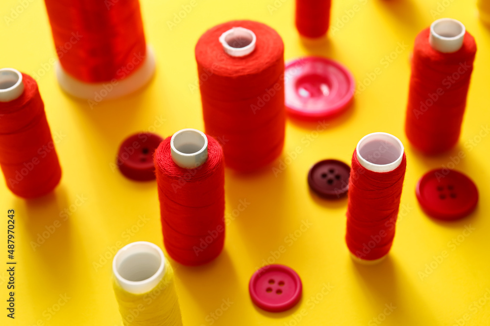 Thread spools and buttons on yellow background, closeup