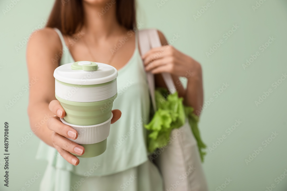 Young woman with eco bag and cup of coffee on green background, closeup