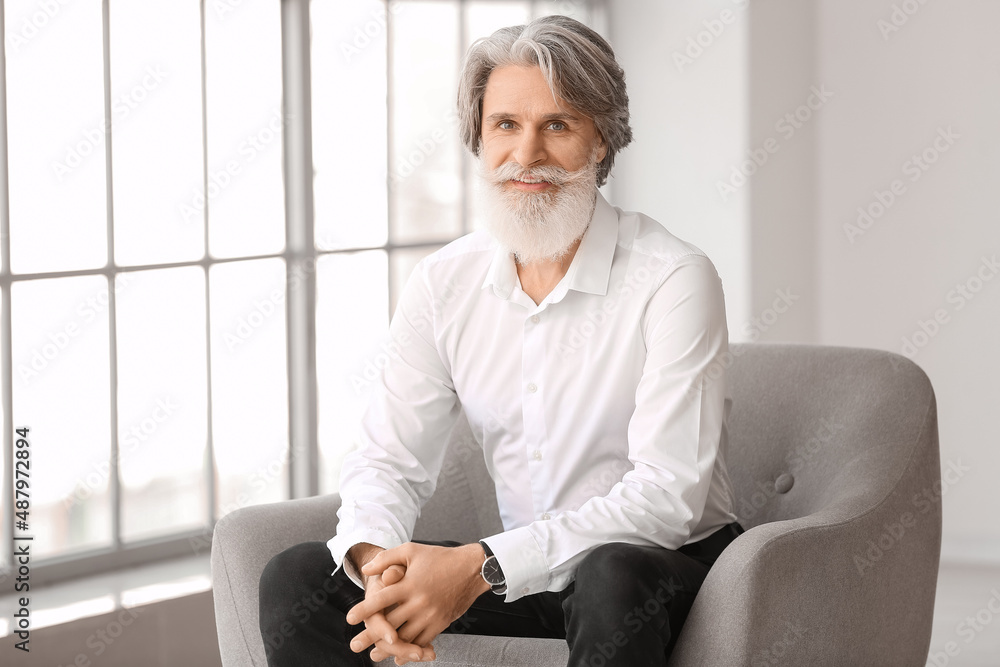 Portrait of handsome mature bearded man sitting in armchair at home