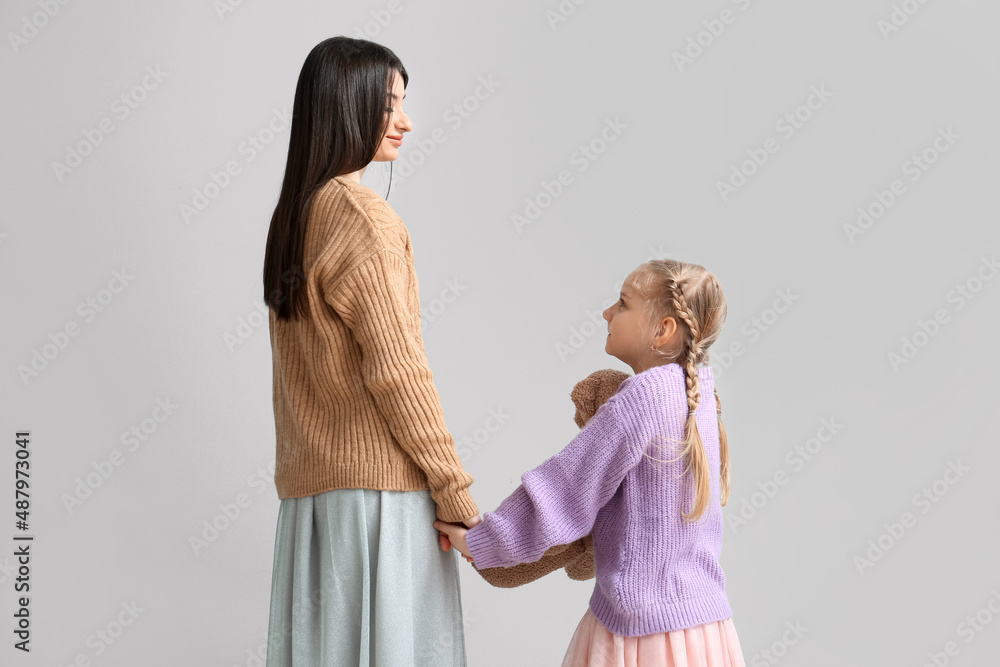 Little girl and her mother in warm sweaters holding hands on light background