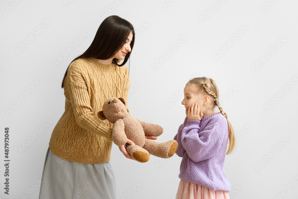 Happy mother giving toy to her little daughter on light background