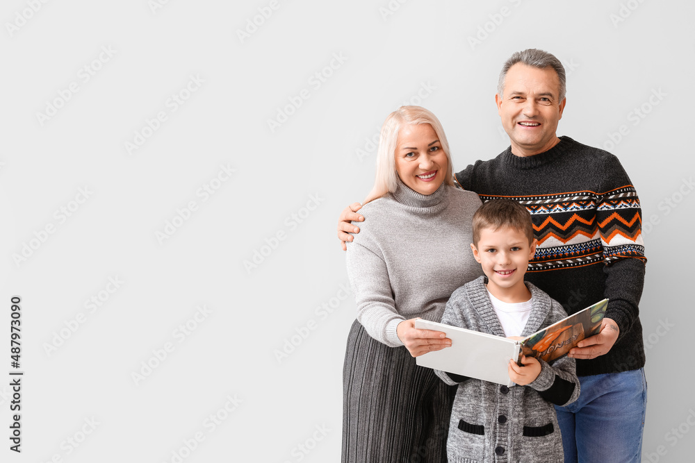 Little boy with his grandparents in warm sweaters reading book on light background