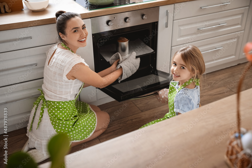 Little girl and her mother taking baking dish with Easter cake from oven in kitchen