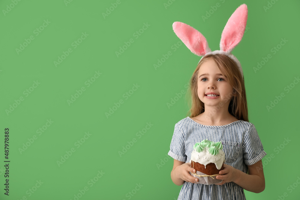 Little girl in bunny ears with tasty Easter cake on green background