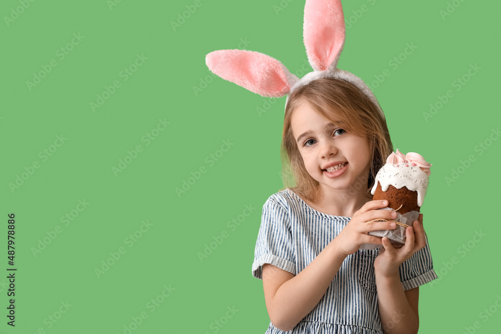 Little girl in bunny ears with tasty Easter cake on green background