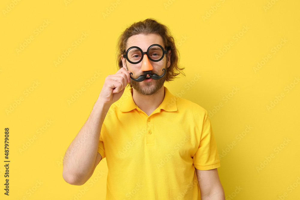 Funny young man in disguise on yellow background. April fools day celebration