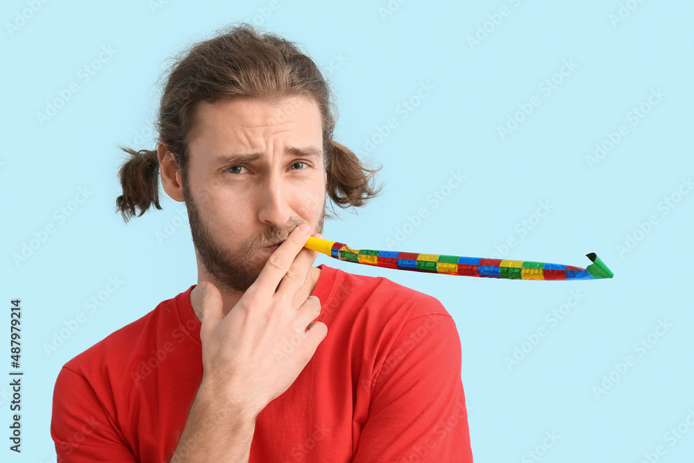 Funny young man with party whistle on blue background. April fools day celebration