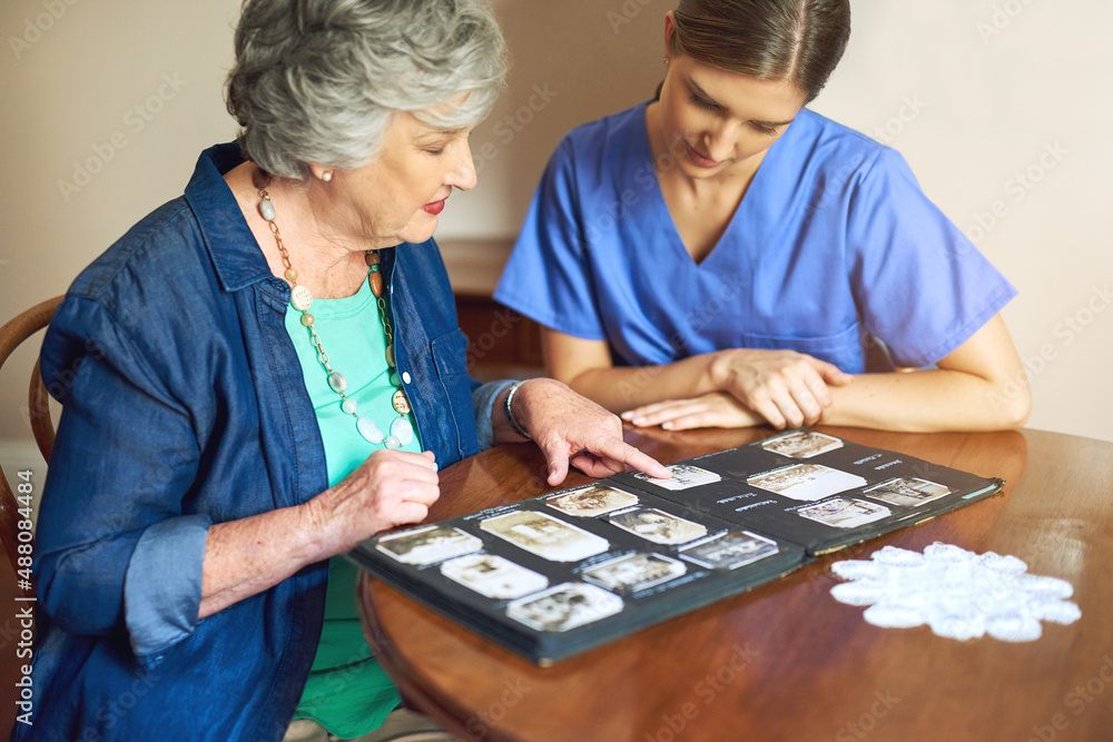 Shes got plenty of photos to share. Shot of a resident and a nurse looking through a photo album.