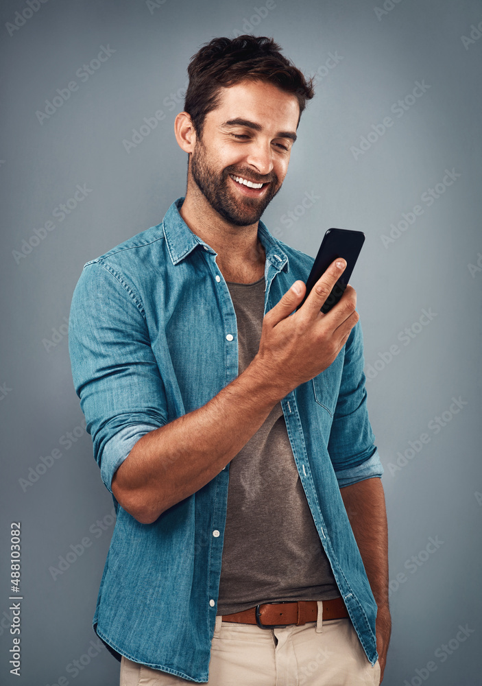 The text that put a smile on his dial. Studio shot of a handsome young man using a mobile phone agai