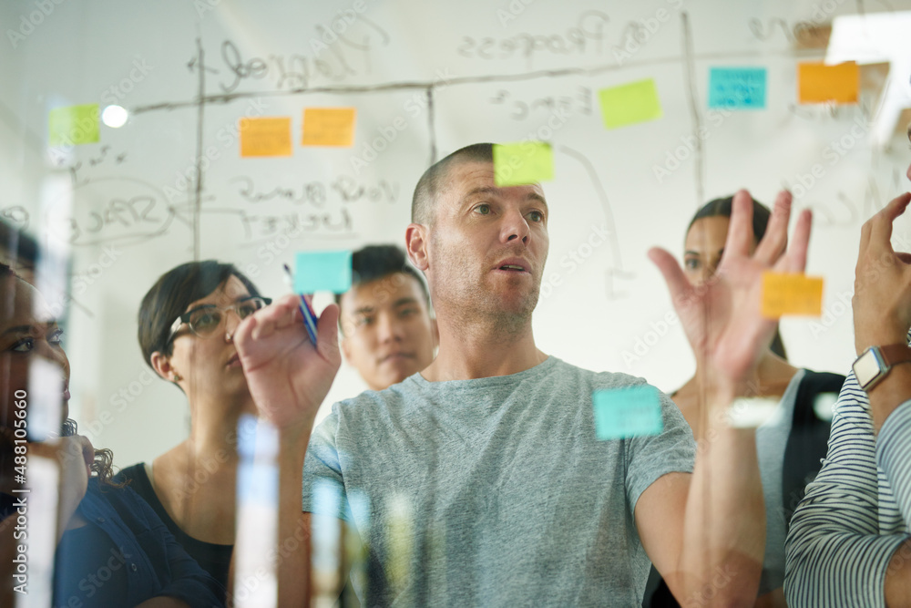 Planning is the first step. Cropped shot of a group of young designers planning on a glass board.