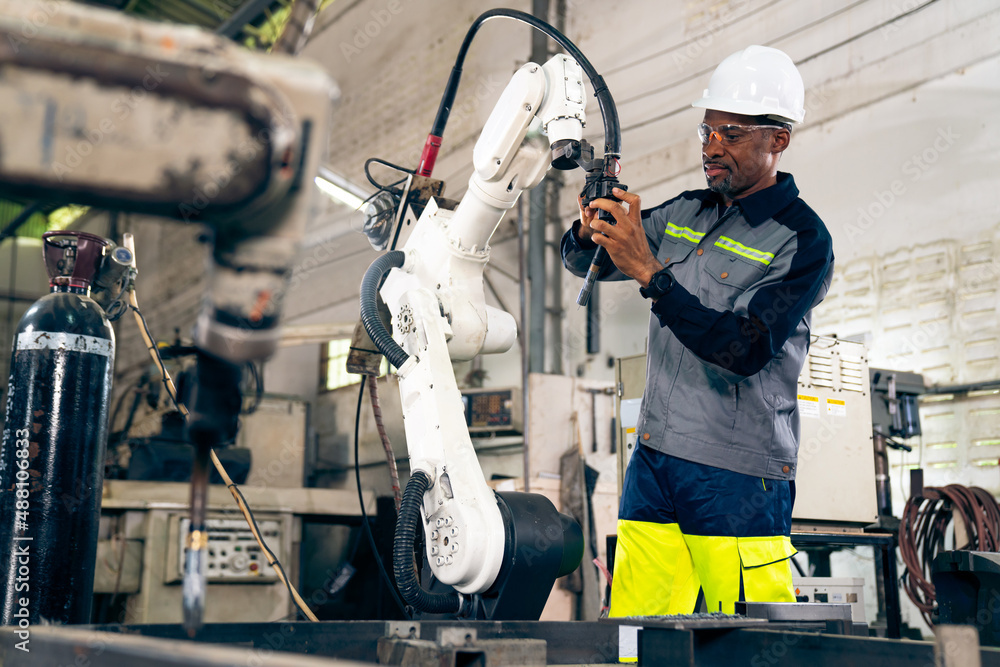 African American factory worker working with adept robotic arm in a workshop . Industry robot progra