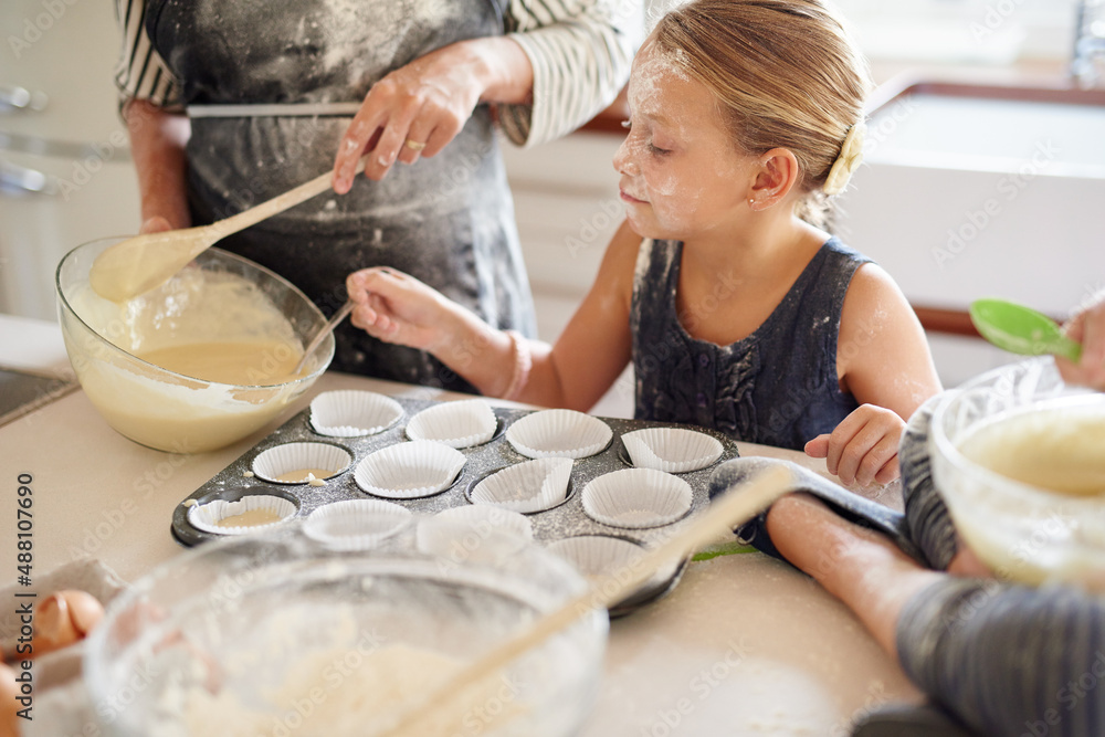 Almost ready for the over. Shot of two little girls baking with their mother in the kitchen.