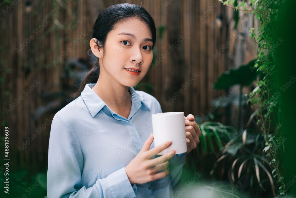 美丽的年轻亚洲女人在花园里放松，喝茶