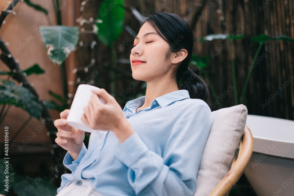 美丽的年轻亚洲女人在花园里放松并喝茶