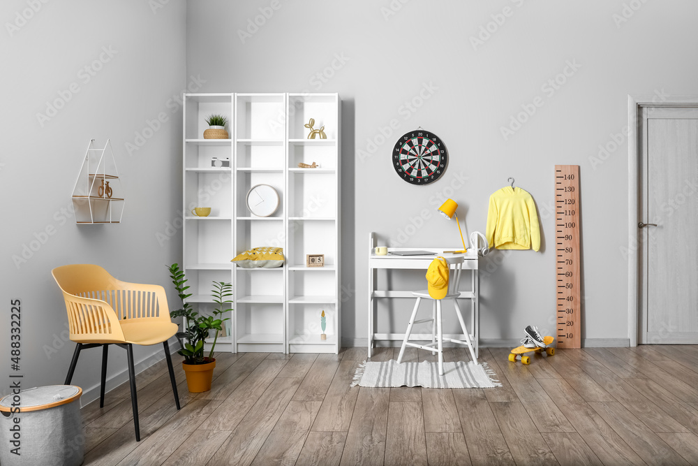 Interior of light childrens room with workplace, shelving unit and dartboard