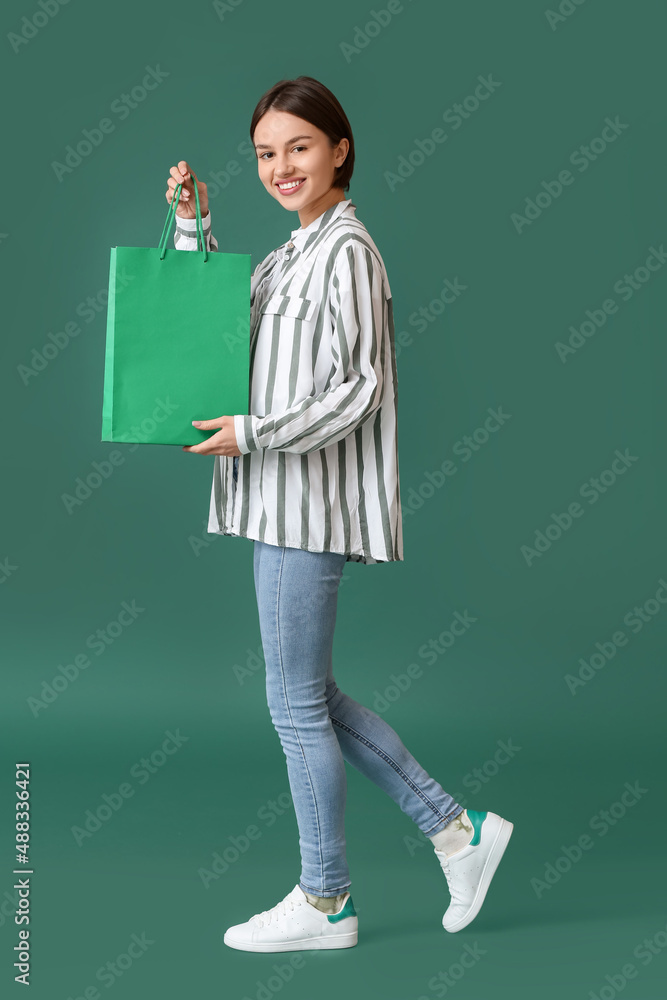 Young woman with shopping bag on green background