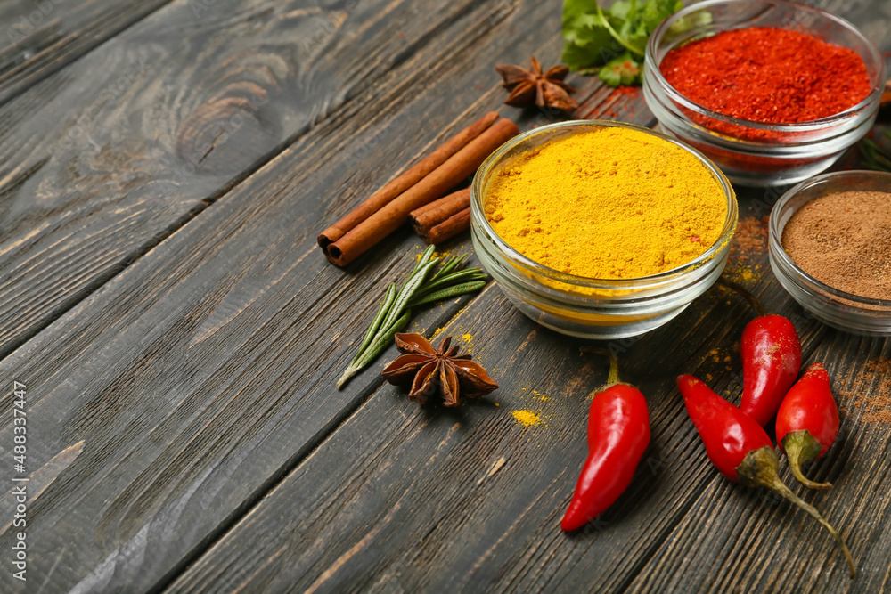 Glass bowls with aromatic spices on dark wooden background