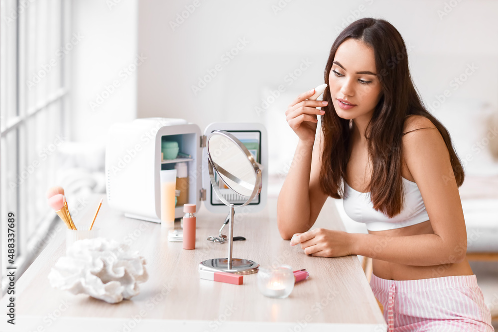 Beautiful young woman applying makeup at dressing table at home