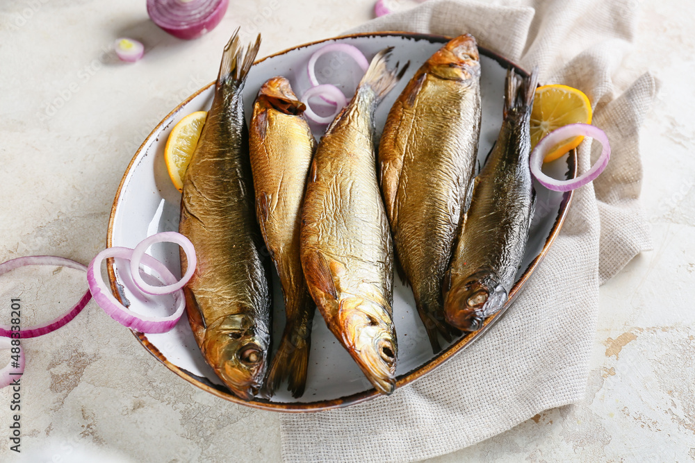 Plate with smoked herring fishes on light background