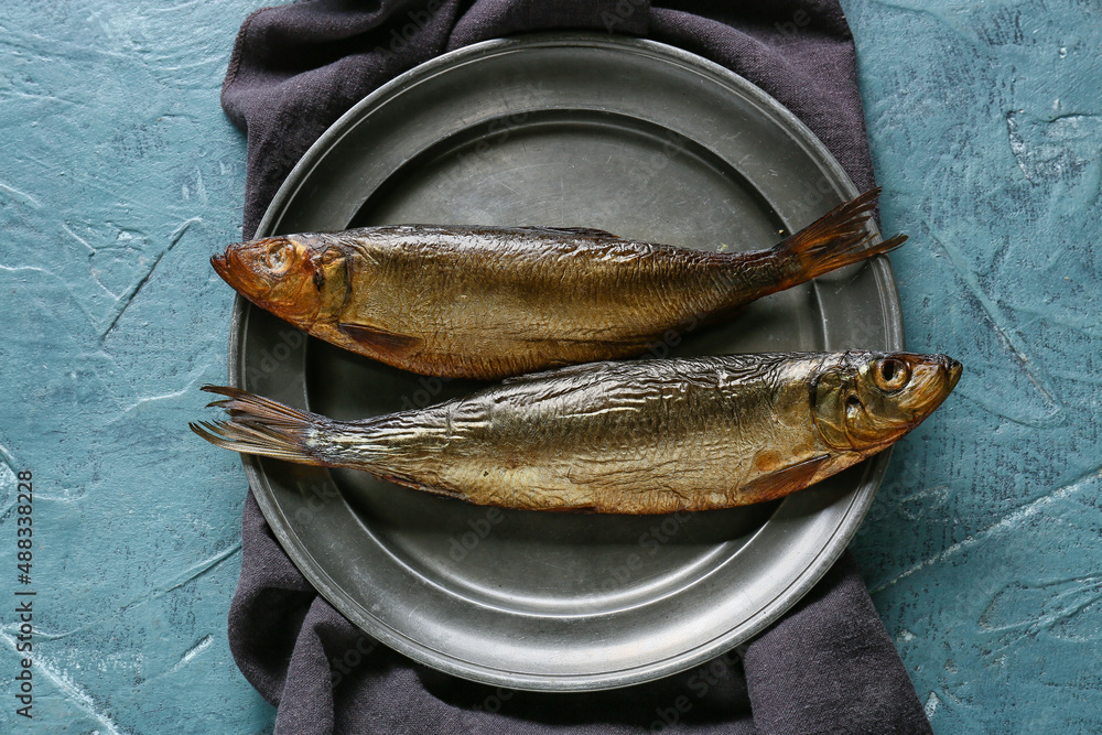 Plate with smoked herring fishes on blue background