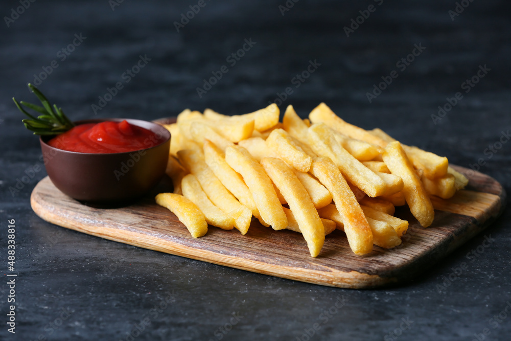 Wooden board with tasty french fries and ketchup on black background