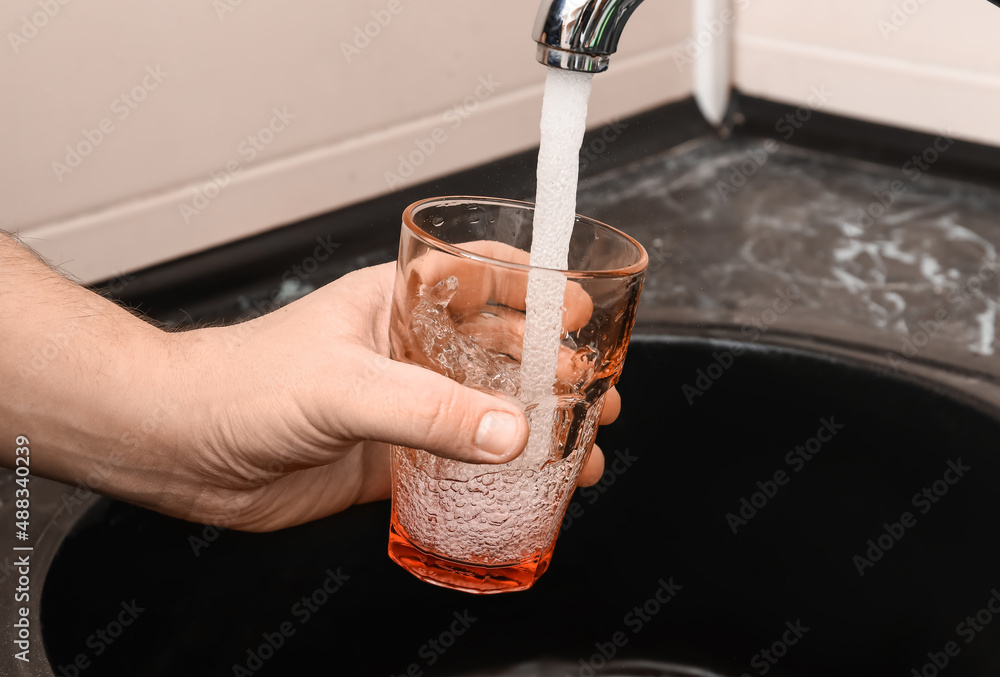 Man filling glass with water from tap in room, closeup