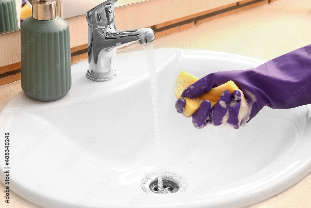 Woman in rubber glove with cleaning sponge near ceramic sink, closeup