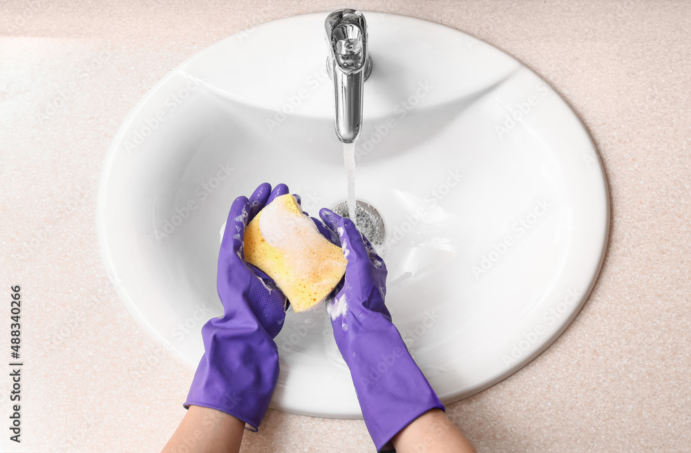 Woman in rubber gloves with cleaning sponge near ceramic sink, closeup