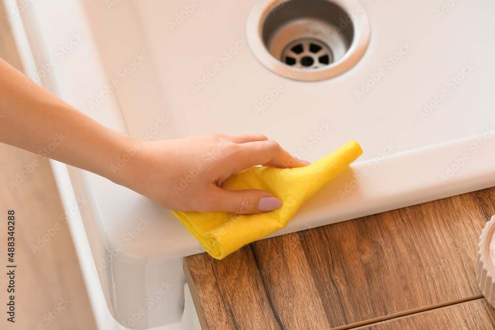 Housewife cleaning ceramic sink with rag, closeup