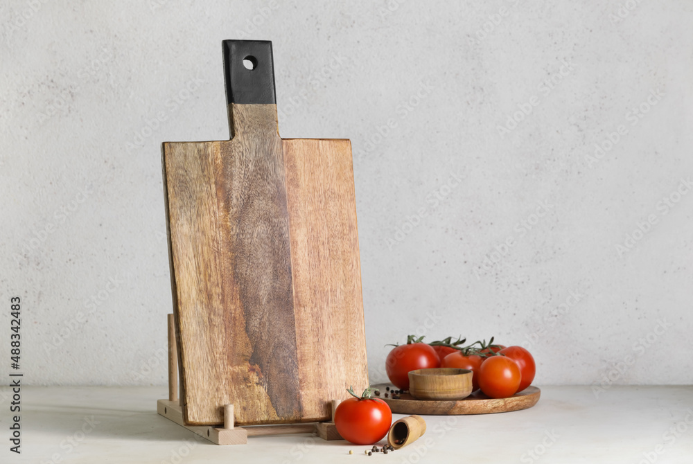 Wooden cutting board and tomatoes on light background