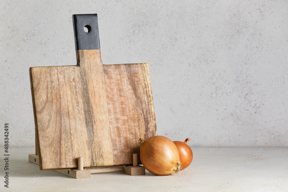 Wooden cutting board and onion on light background