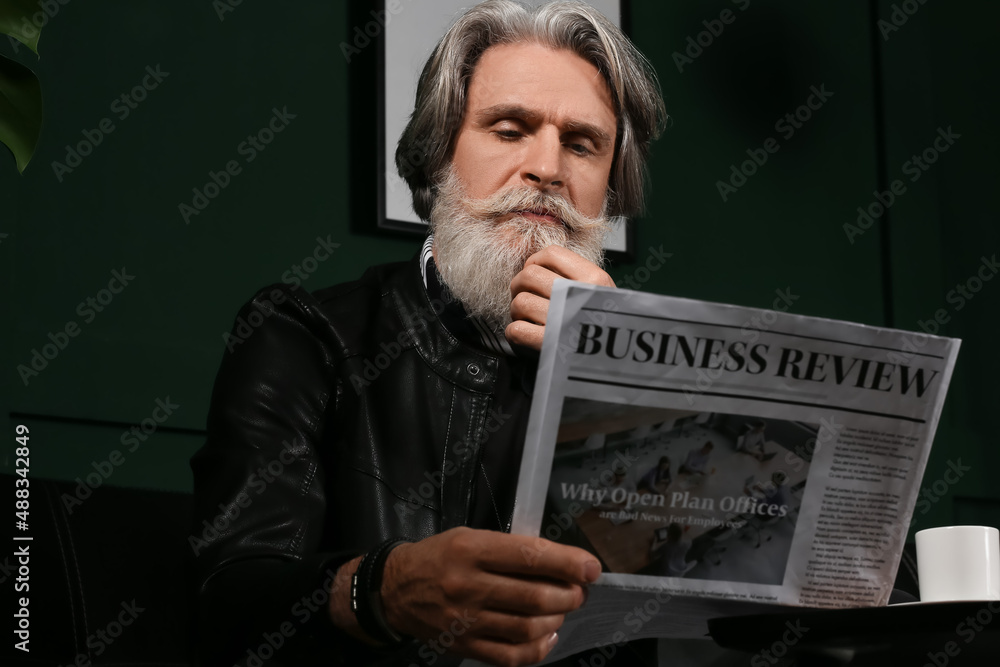 Handsome mature bearded man reading newspaper at home