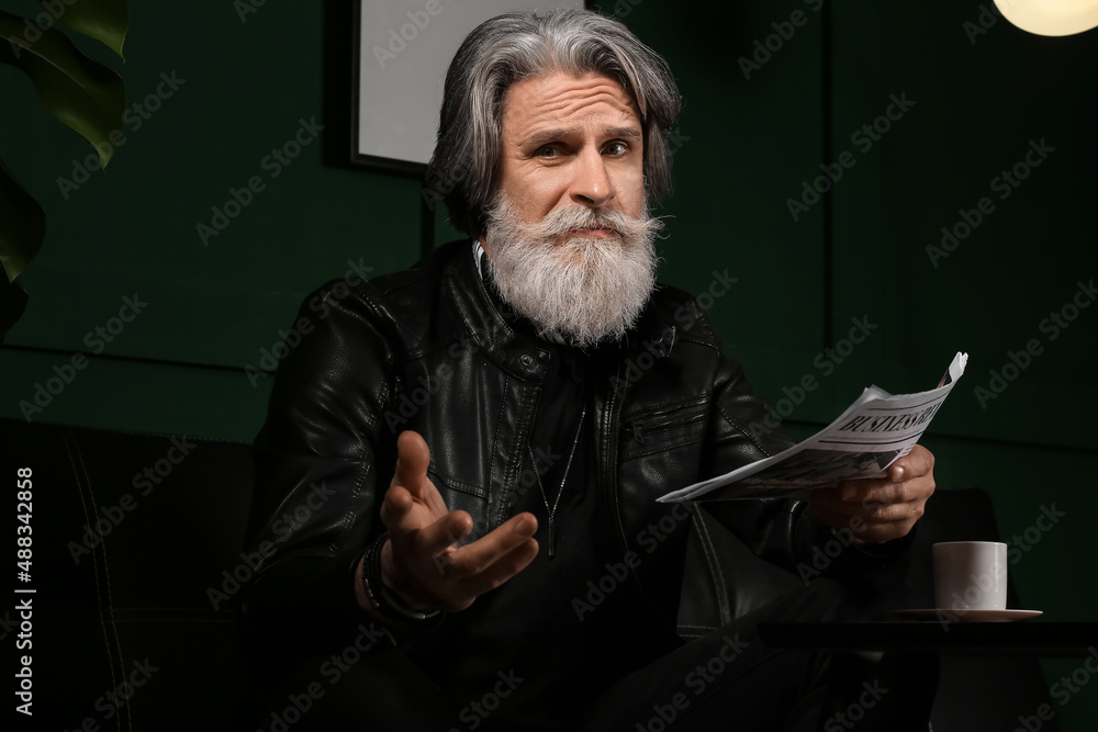 Handsome mature bearded man reading newspaper at home