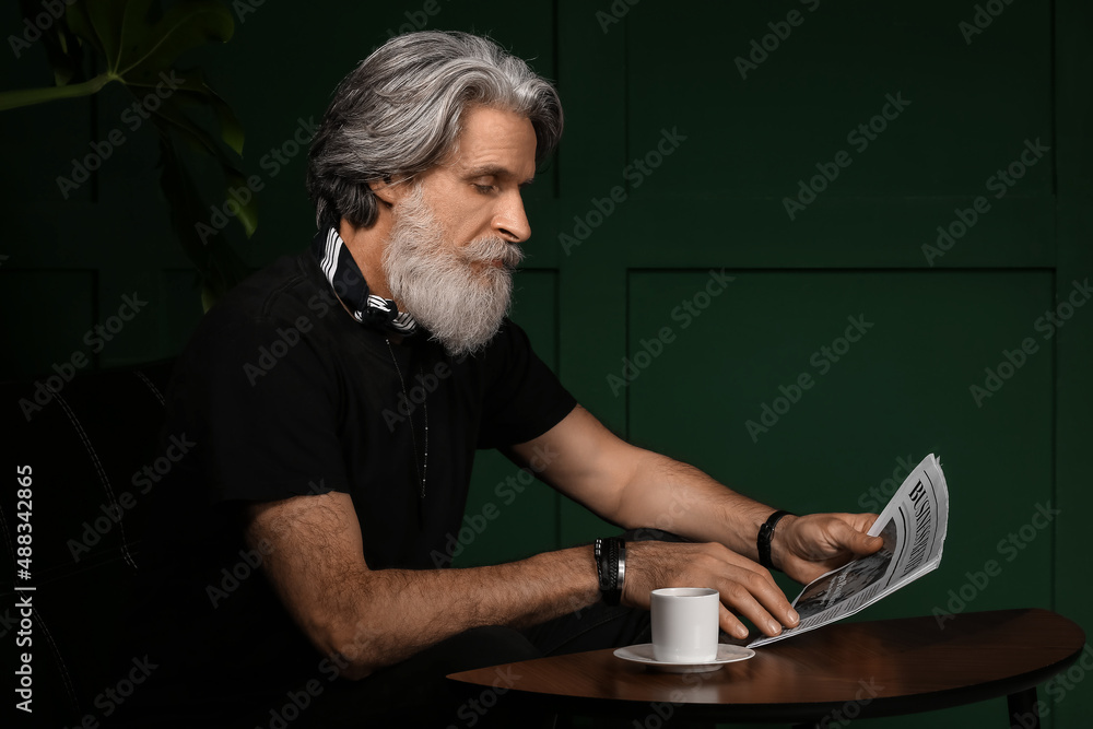 Handsome mature bearded man reading newspaper at home