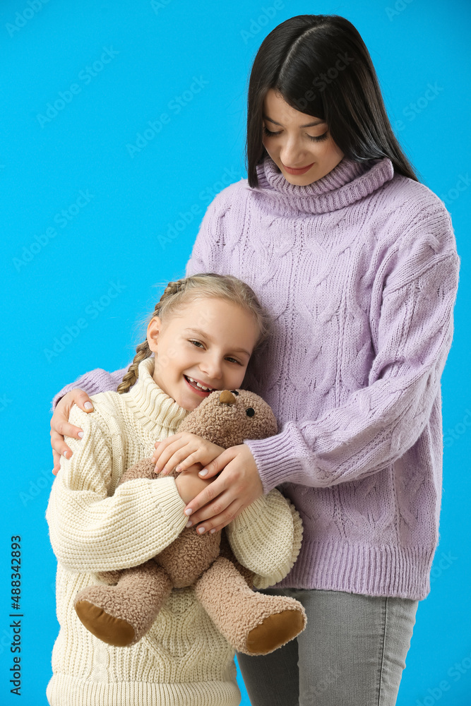 Little girl with toy and her mother in warm sweaters on blue background