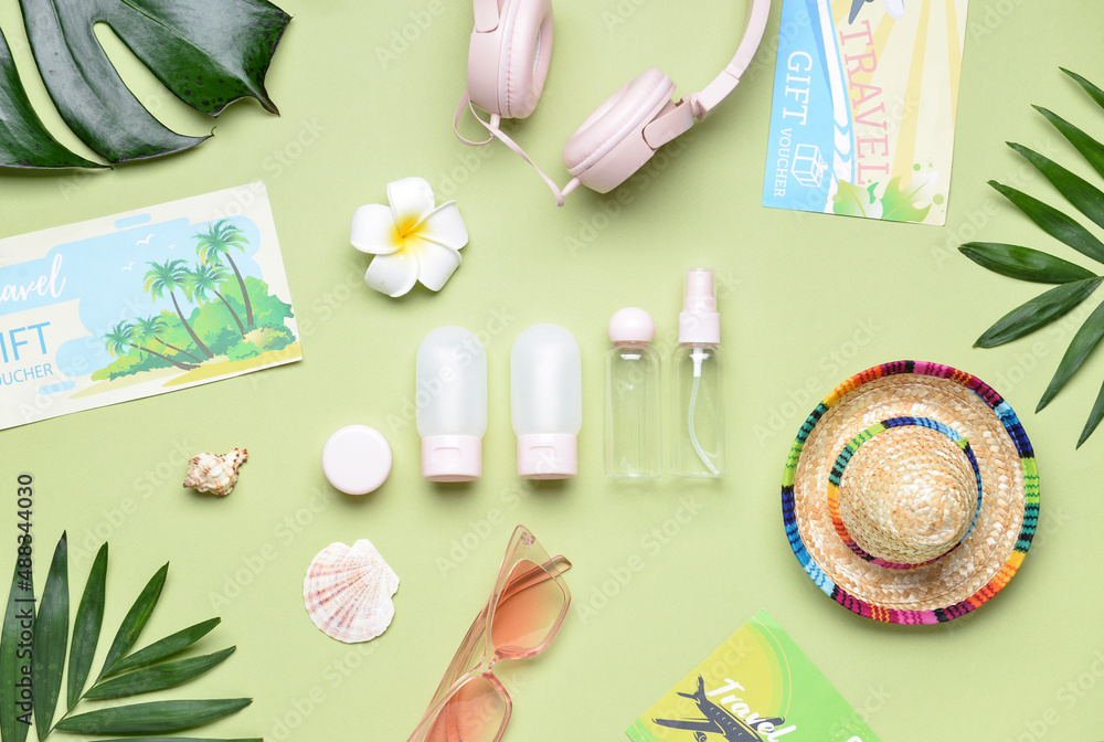 Composition with travel cosmetic bottles, beach accessories and palm leaves on green background