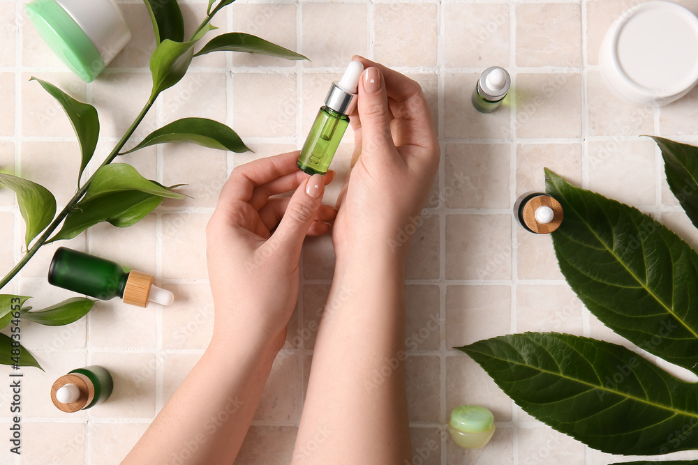 Female hands with bottle of serum on light tile background