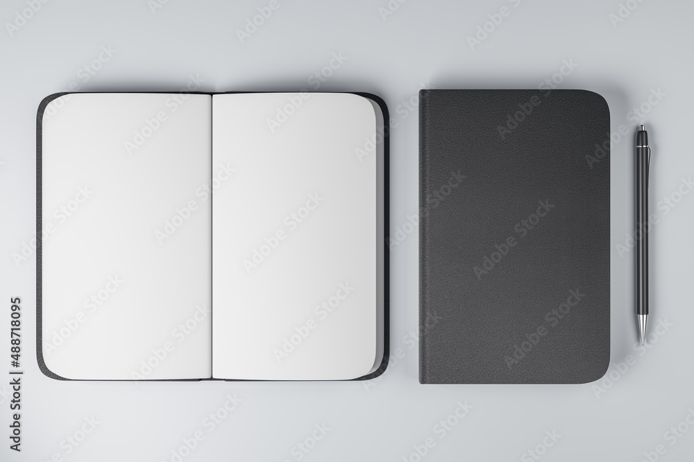 Top view on notebooks with black cover and blank white pages and black pen near on light background.