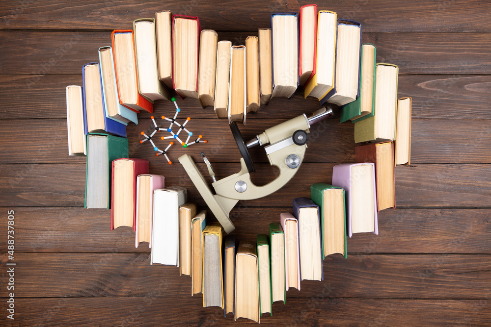 Love science concept. Heart shape of books, microscope and molecule model on wooden desk. Take a deg